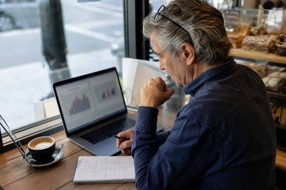 Small business owner comparing two job ad budgets on a laptop at a cafe table